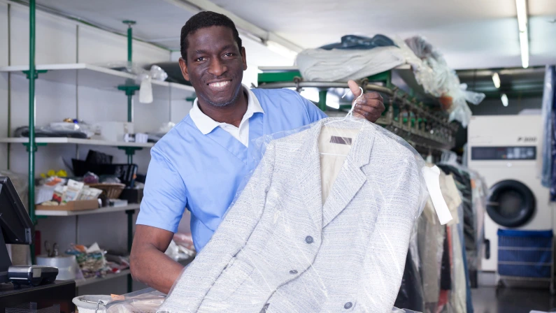 Happy African American worker of laundry offering professional dry cleaning, showing clean clothing