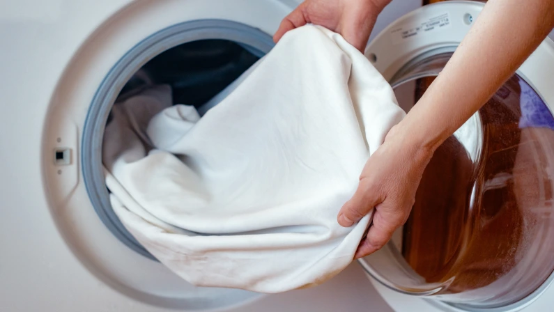 Close-up of women's hands pulling clean white linen clothes out of the washing machine after washing in the bathroom.Women's hands put the laundry in the washing machine.Routine homework.Laundry day.