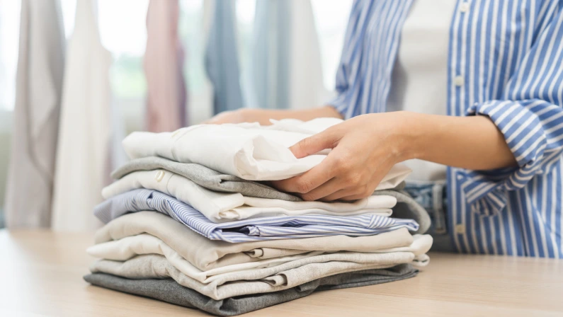Feel softness, chore of asian young woman, girl hand holding pile clothing from table, stack folding clean clothes after washing, laundry and dry. Household working at home. Laundry of maid concept.