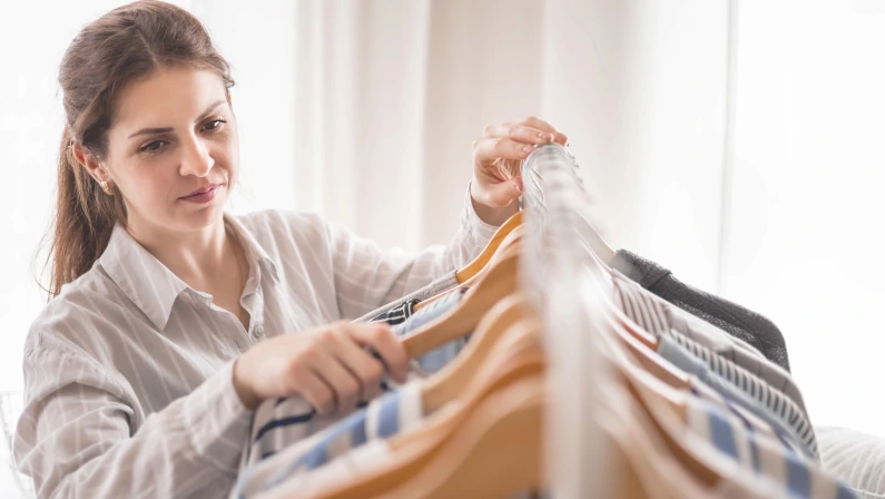 Beautiful light wardrobe with women's clothing. The girl hangs up and puts things in order in the closet. Clothes storage.