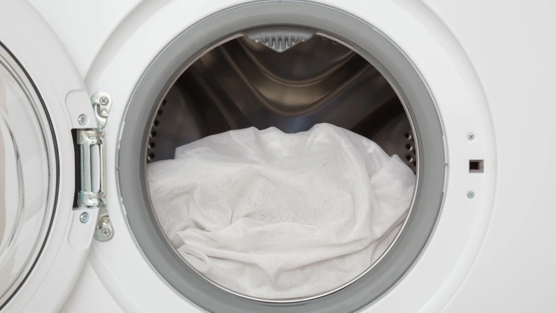 White day transparent curtains in opened washing machine. Closeup. Front view.