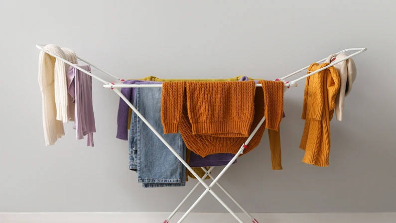 Clean winter clothes hanging on dryer near light wall