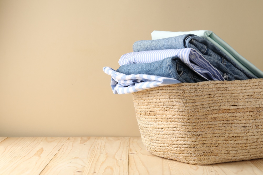 Laundry basket with clothes on wooden table near beige wall indoors, closeup. Space for text