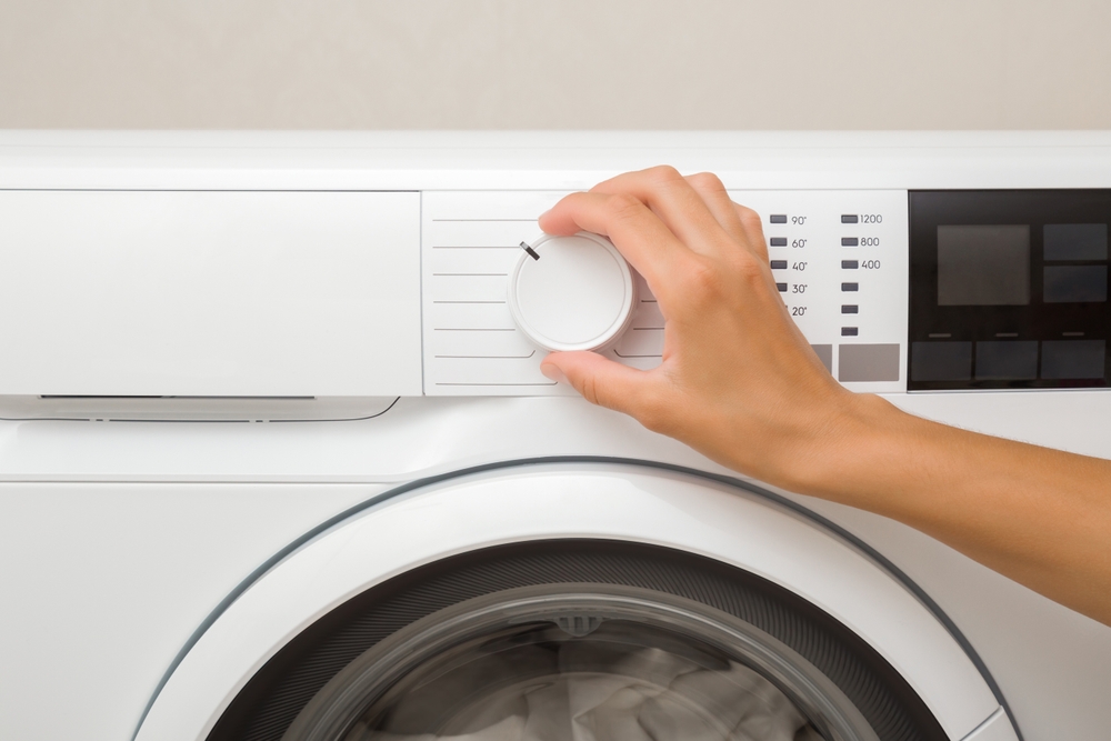 Young adult woman hand finger turning button on white washing machine