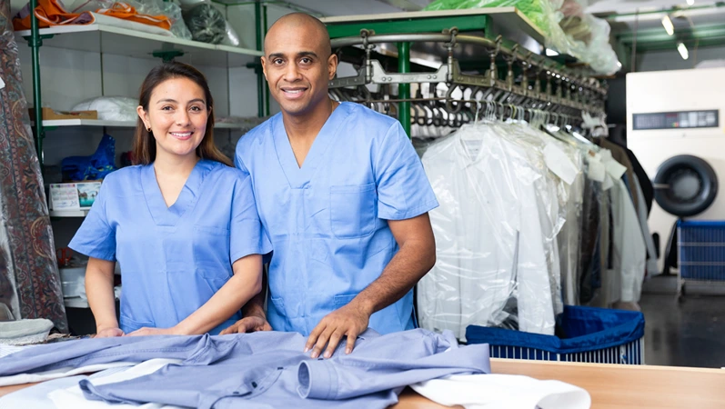 Two smiling workers offering professional dry cleaning, showing clean clothing