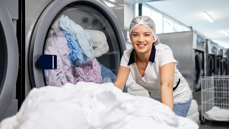 Working in hospital dry cleaning service. Portrait of smiling laundry worker by washing machine.