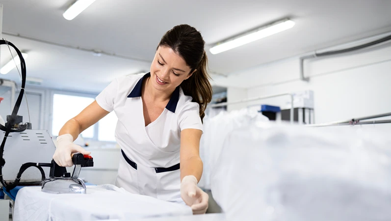 Professional female worker ironing clothes in laundry service.