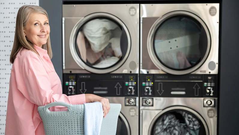Retired female in laundromat using commercial machines for washing and drying