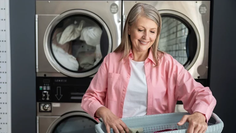 Senior woman washing clothes in laundromat using coin-operated machines for convenience