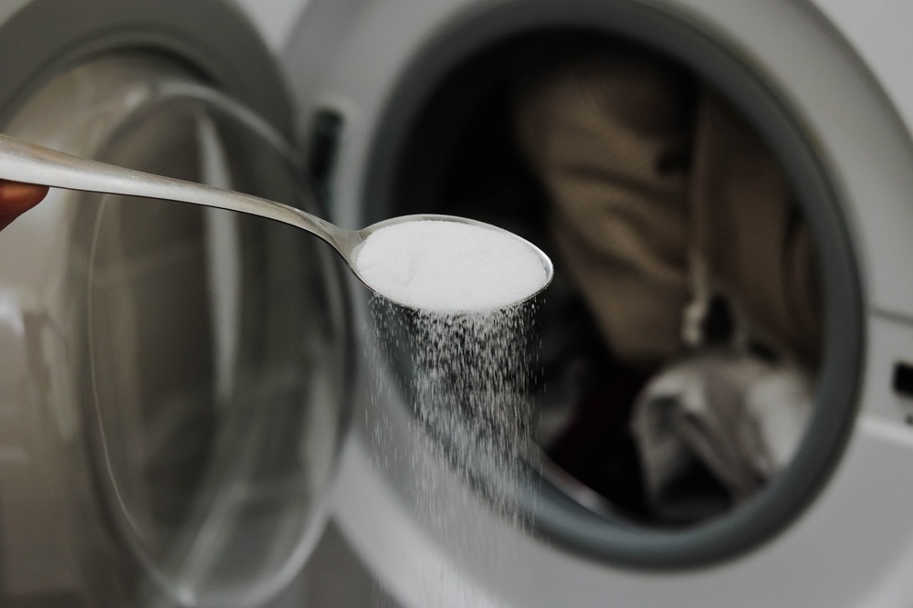 Spoon with baking soda in front of a washing machine