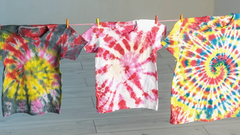 Tie dye-style T-shirts hung on a clothesline. Making clothes at home. Flat lay.