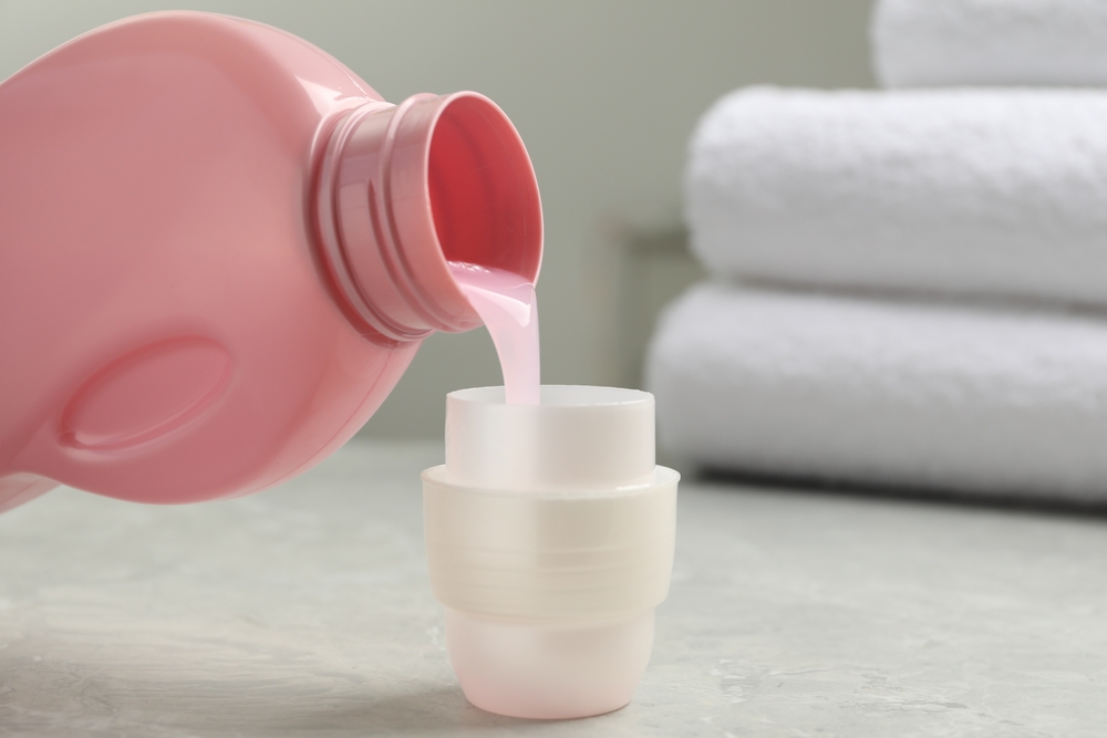 Pouring laundry detergent from bottle into cap on light grey marble table, closeup