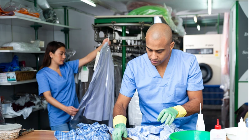 Focused man drycleaner removing spots and stains cleaning shirt with brush