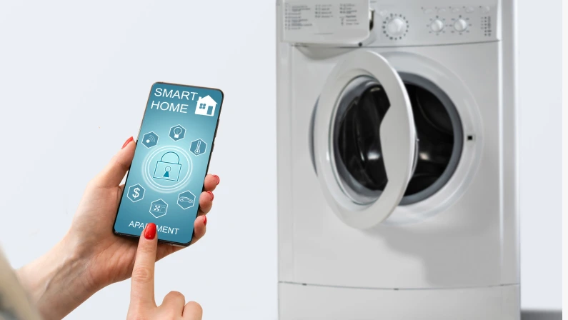 Close-up Of Woman Hand Using Mobile Phone App To Operate Smart Washing Machine