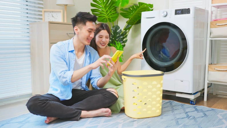 asian couple is using phone to control the washing machine when cleaning clothes
